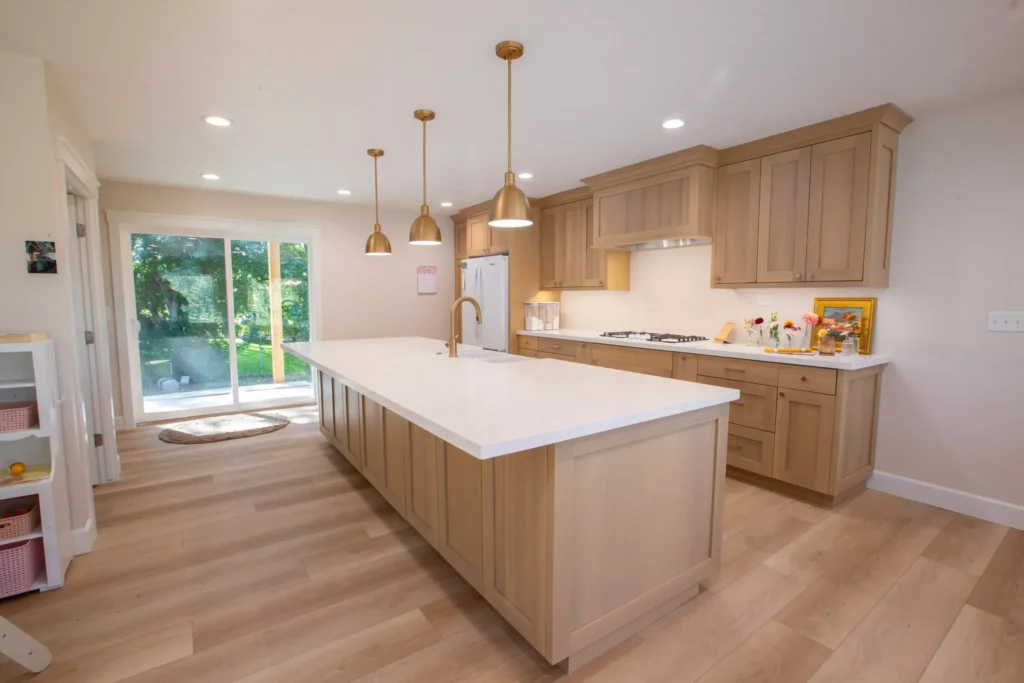Modern kitchen with wooden flooring solutions, light wood cabinets, large island, and pendant lights